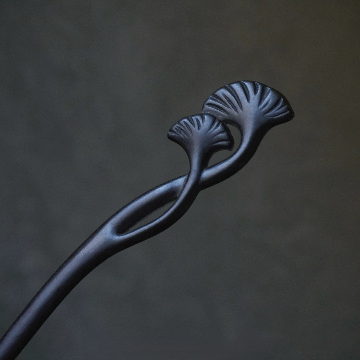 Natural African Blackwood hair stick with ginkgo leaf (xing shi) design against blurred dark background.