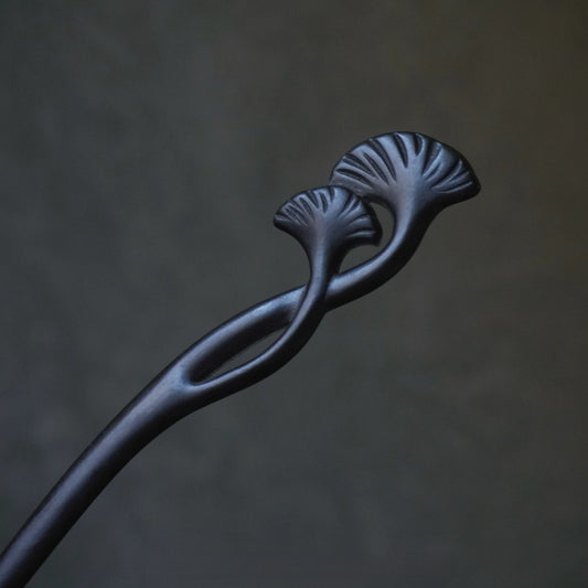 Natural African Blackwood hair stick with ginkgo leaf (xing shi) design against blurred dark background.