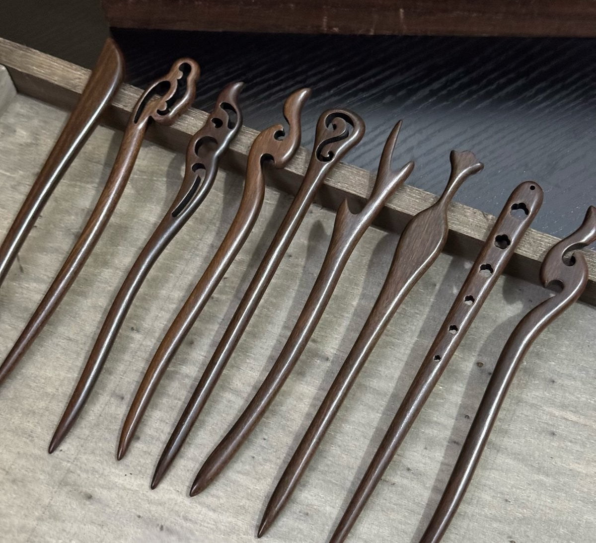 Set of 10 natural rosewood hair sticks with carved designs, approx. 18cm length, arranged in wooden tray.