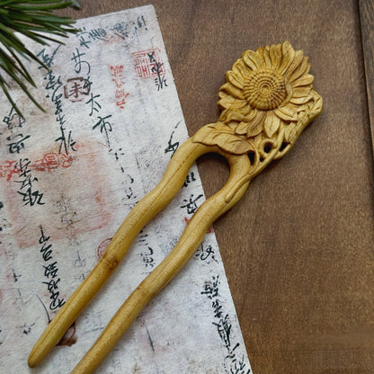 Natural peach wood hair fork with sunflower design on textured paper background