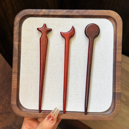 Set of three natural rosewood hair sticks with star, moon, and circle celestial designs displayed in wooden tray
