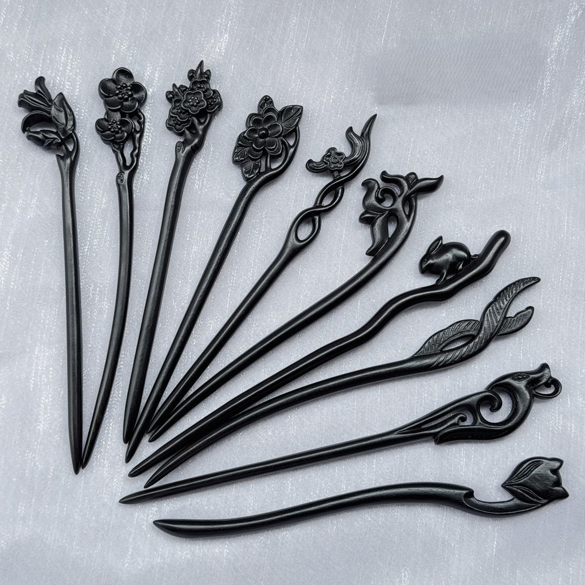 Set of 10 natural African Blackwood hair sticks with carved floral, bird, and animal designs on a light background.