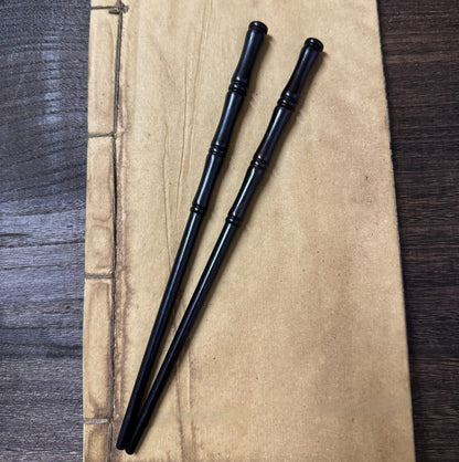 Pair of natural African Blackwood hair sticks with bamboo design 17cm on parchment paper background.