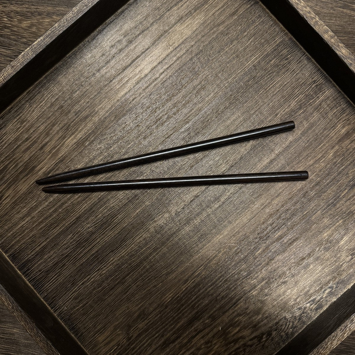 Pair of natural African Blackwood hair sticks with chopstick (kuai niang) design 18cm on wooden tray.