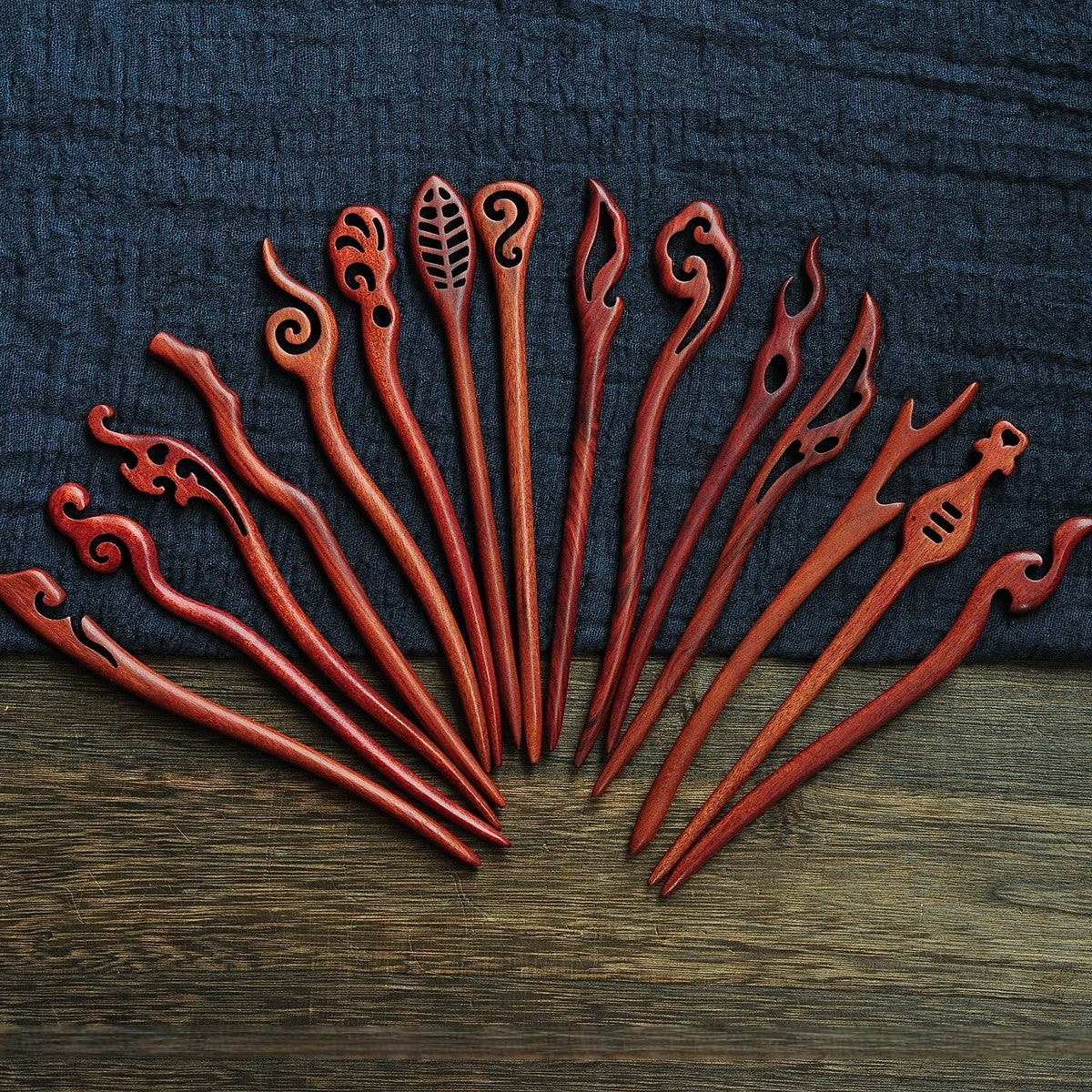 Set of natural red sandalwood 18cm hair sticks with assorted carved designs arranged on blue fabric background