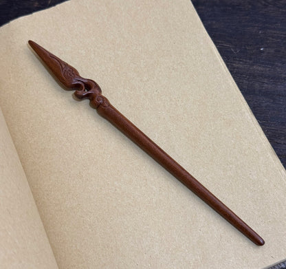 Natural lacewood hair stick with Mulan spear design 18cm on open book background.