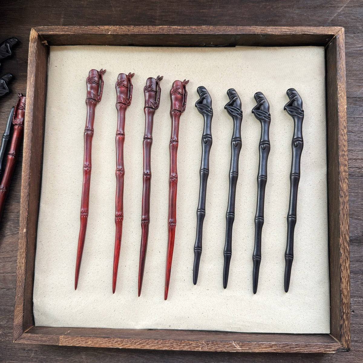 Collection of natural African blackwood hair sticks with bamboo pavilion designs in red and black tones displayed in a wooden tray