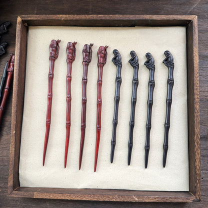 Collection of natural African blackwood hair sticks with bamboo pavilion designs in red and black tones displayed in a wooden tray
