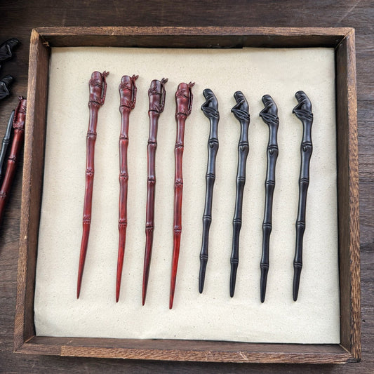 Collection of natural African blackwood hair sticks with bamboo pavilion designs in red and black tones displayed in a wooden tray