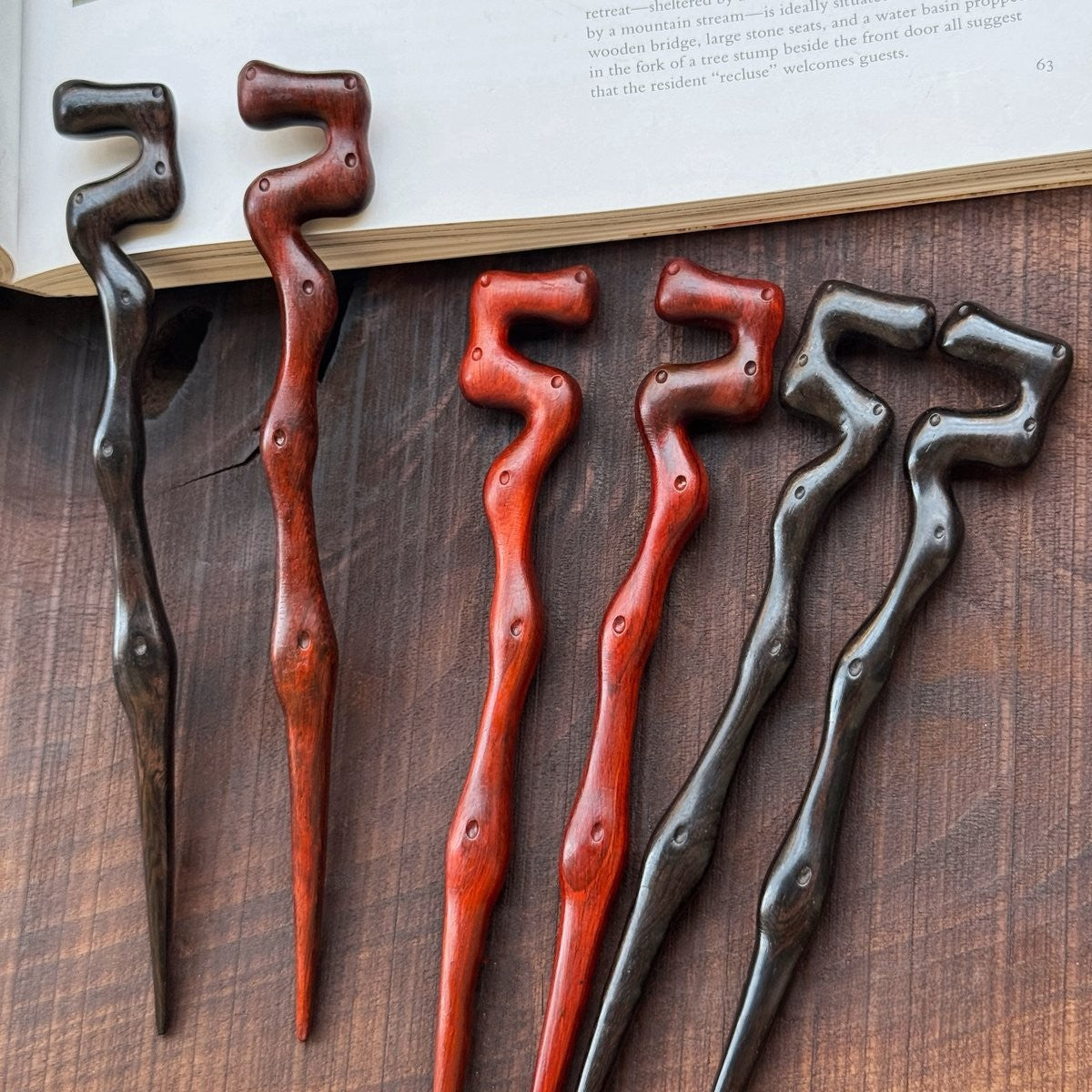 Set of 2 natural African Blackwood hair sticks with Big Dipper (Beidou Qixing) design on wooden surface with open book background.
