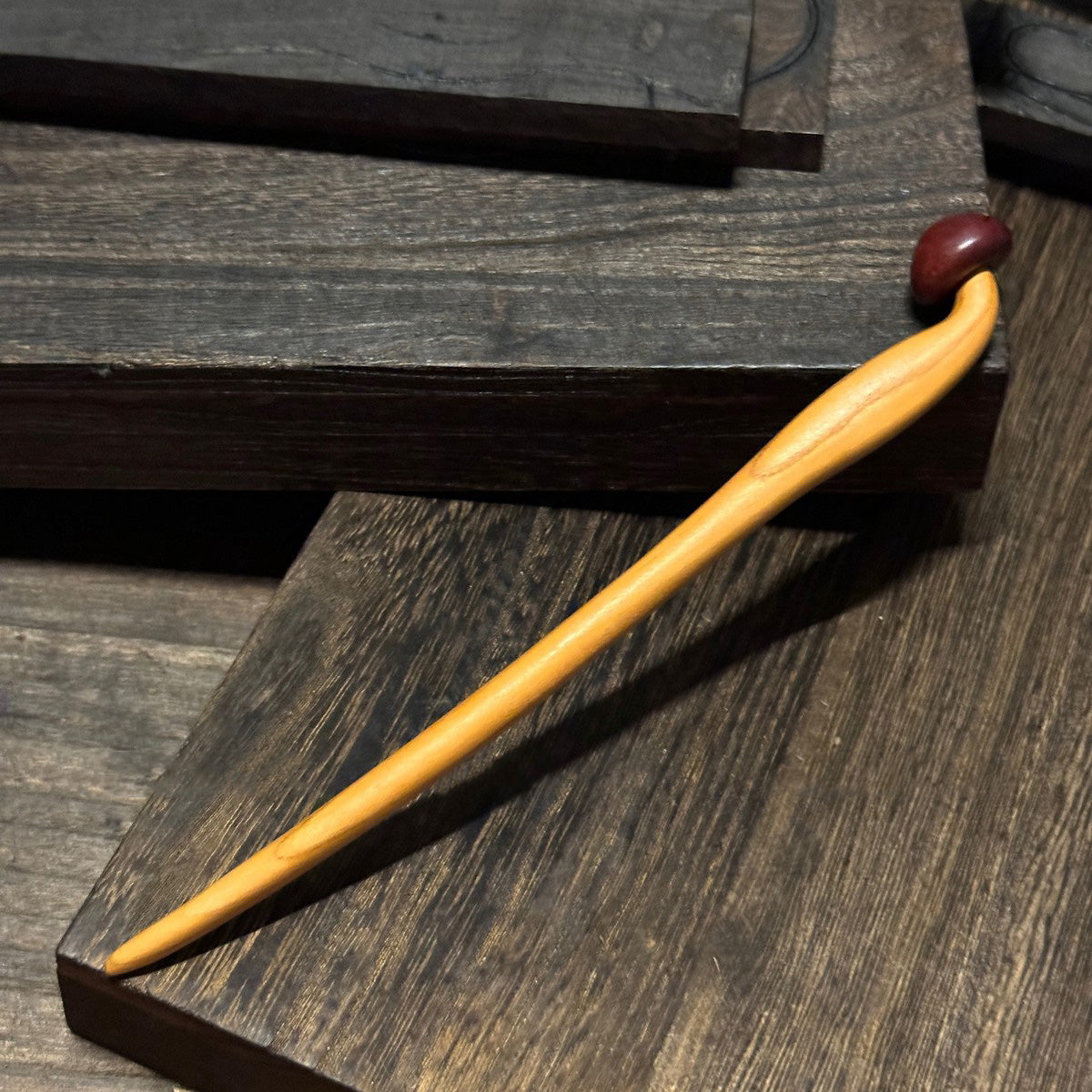 Natural peach wood hair stick with mushroom design placed on dark wooden surface