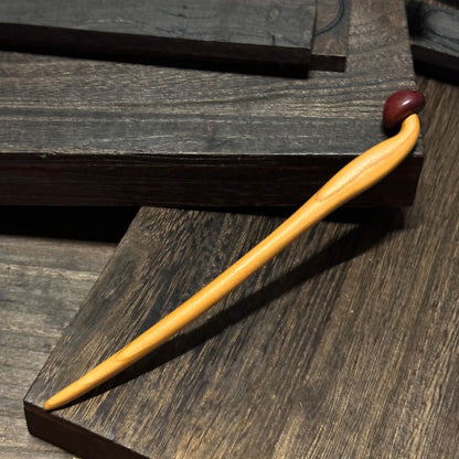 Natural peach wood hair stick with mushroom design placed on dark wooden surface