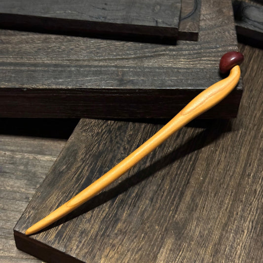 Natural peach wood hair stick with mushroom design placed on dark wooden surface