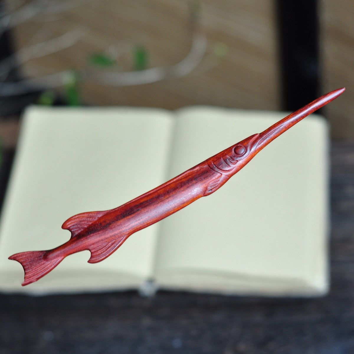 Natural red sandalwood hair stick with swordfish shape design placed on open book