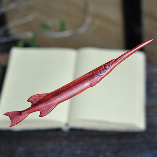 Natural red sandalwood hair stick with swordfish shape design placed on open book