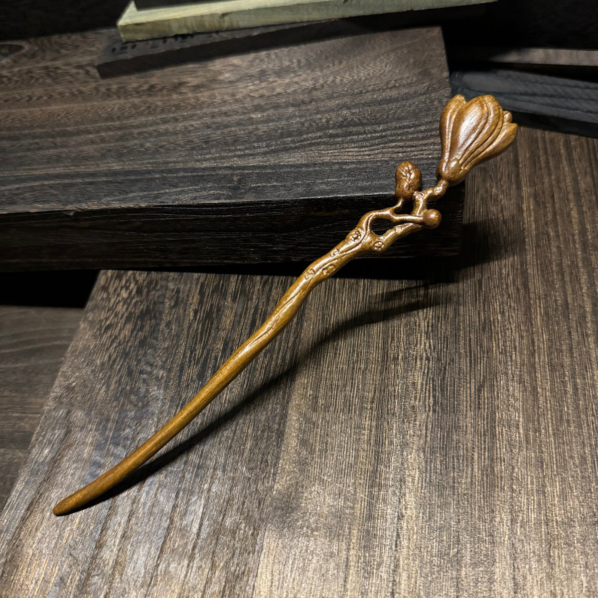 Natural lacewood hair stick with magnolia flower carving 18cm on wooden background.