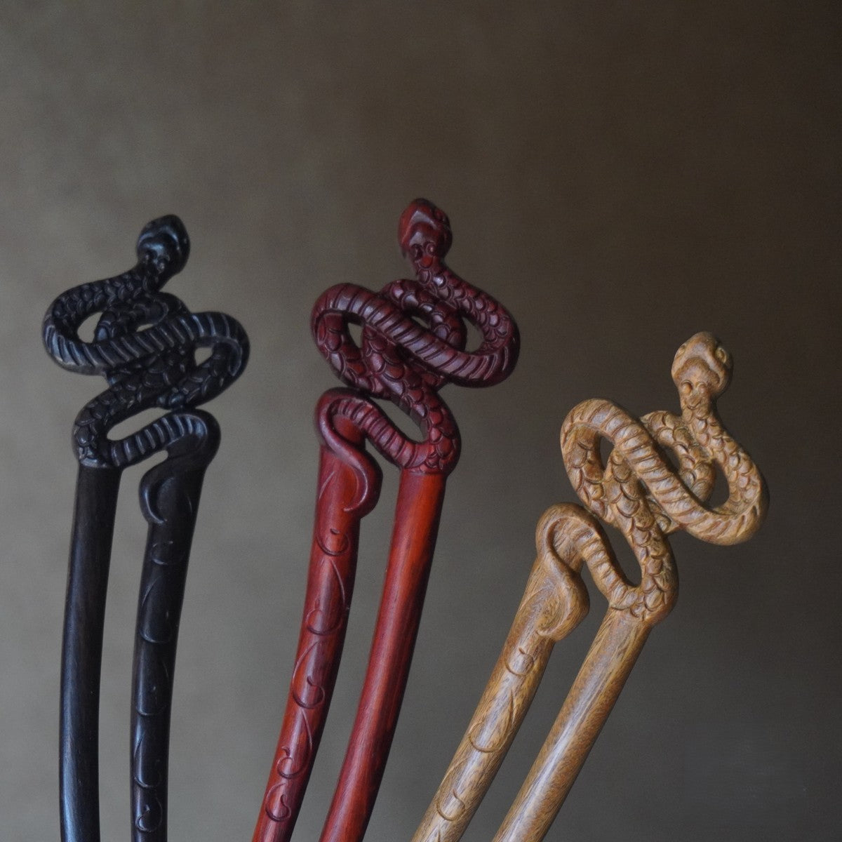Set of three natural wood hair forks with snake design in rosewood, African blackwood, and green sandalwood against neutral background
