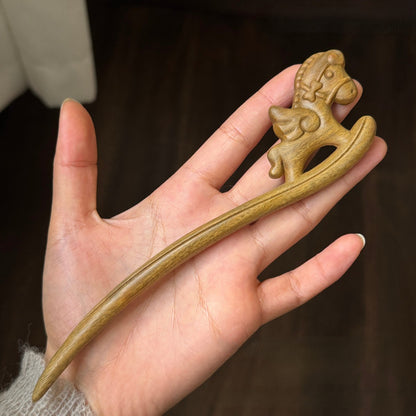 Natural green sandalwood hair stick with rocking horse design held in hand