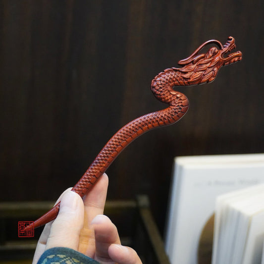 Natural rosewood hair stick with crimson flame dragon design held in hand against dark background