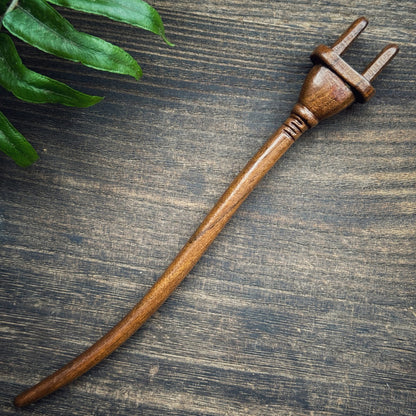 Natural lacewood hair stick with power plug design on dark wooden background with green leaf