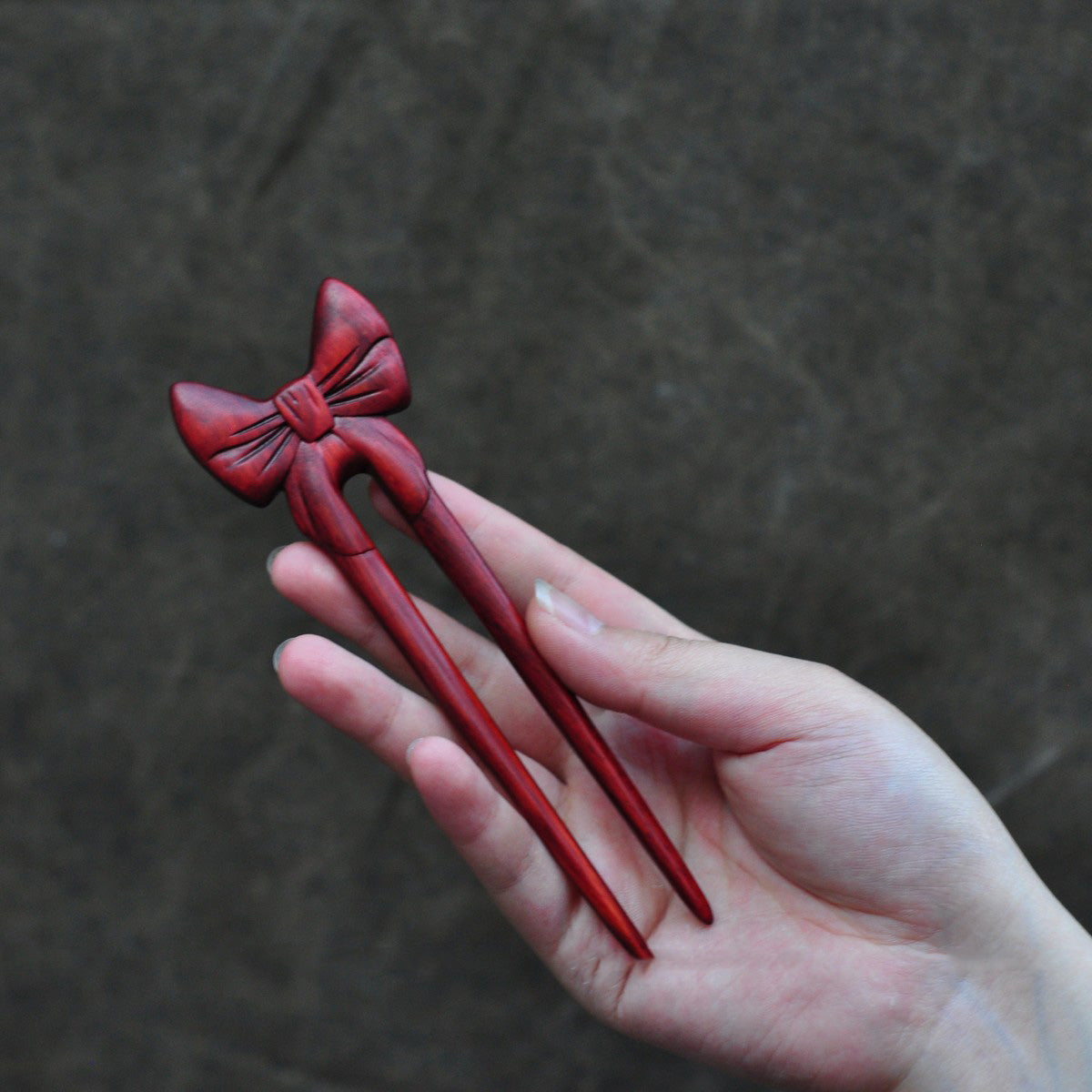 Natural rosewood hair fork with red butterfly bow design held in hand