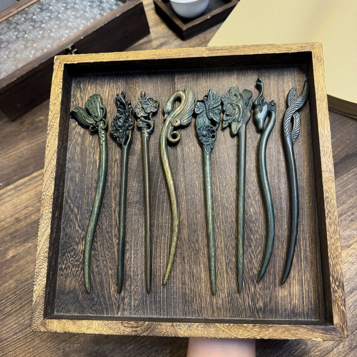 Set of 10 natural Argentine Green Sandalwood hair sticks with carved floral, bird, and animal designs in a wooden box.