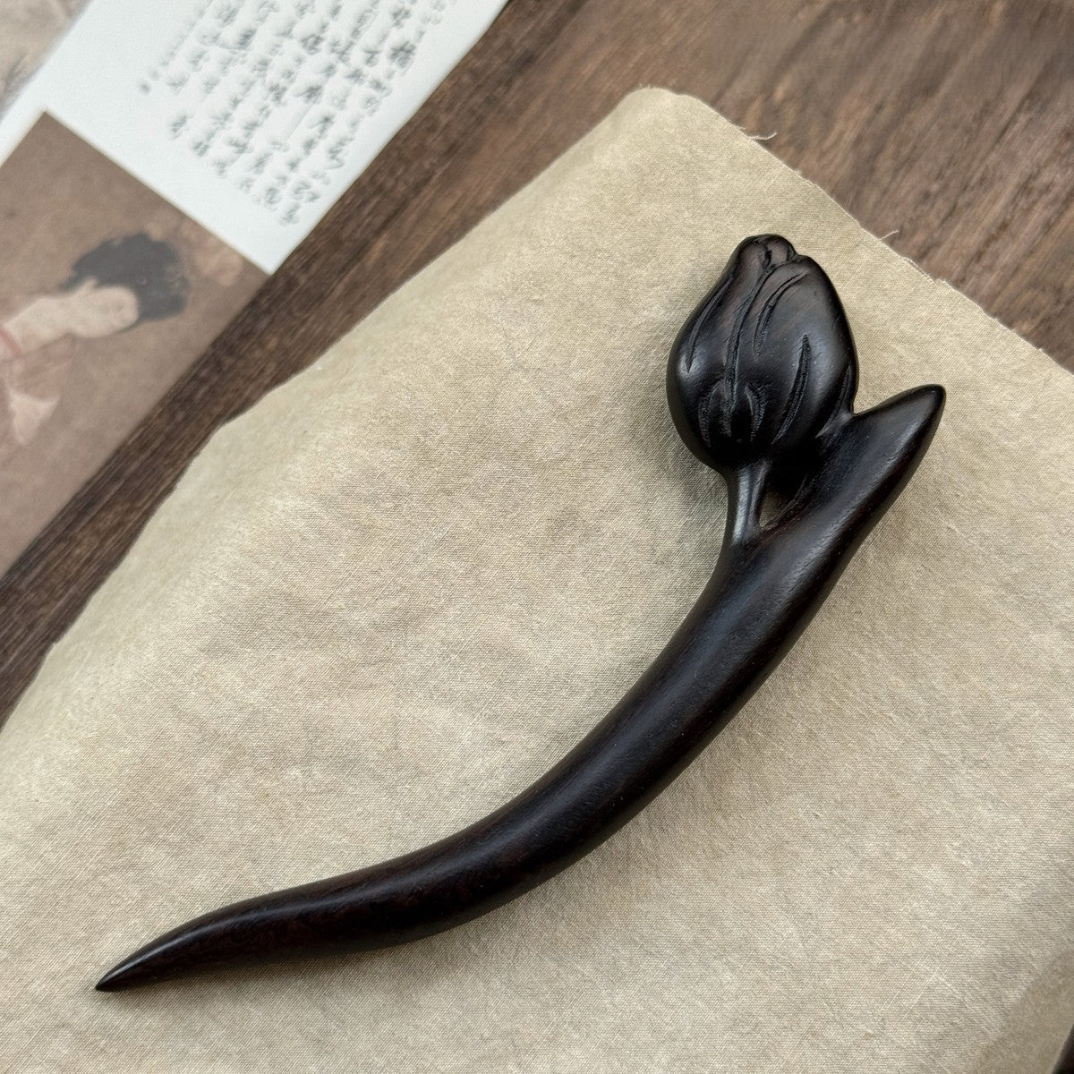 Natural African Blackwood hair stick with tulip flower design 12cm on textured fabric background.