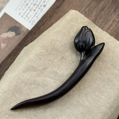 Natural African Blackwood hair stick with tulip flower design 12cm on textured fabric background.
