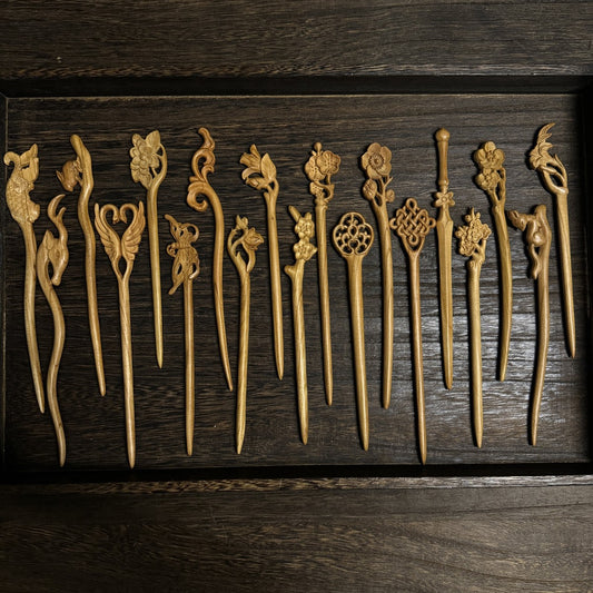 Set of natural aged peach wood hair sticks with assorted floral and nature carvings arranged in wooden tray