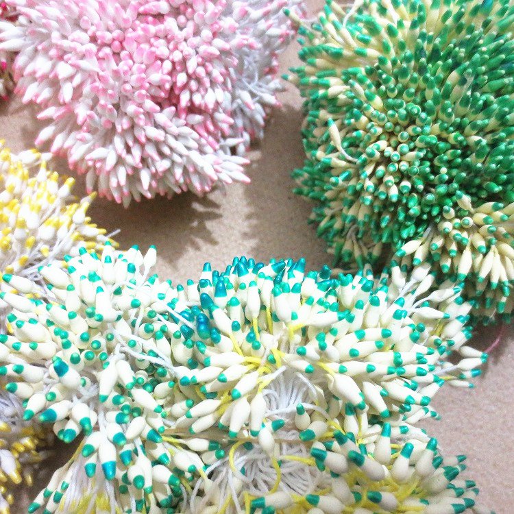 Several double-headed white flower stamens with purple tips, lying separated on a green gridded cutting mat.