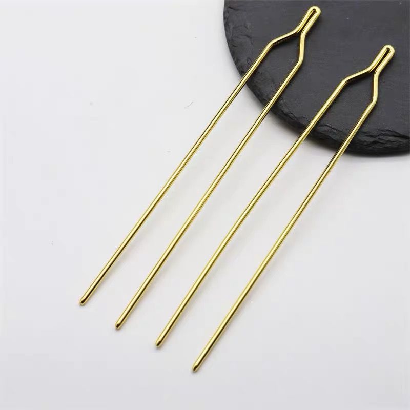Two long Y-shaped metal hair sticks in a polished gold finish, laid on a dark slate surface.