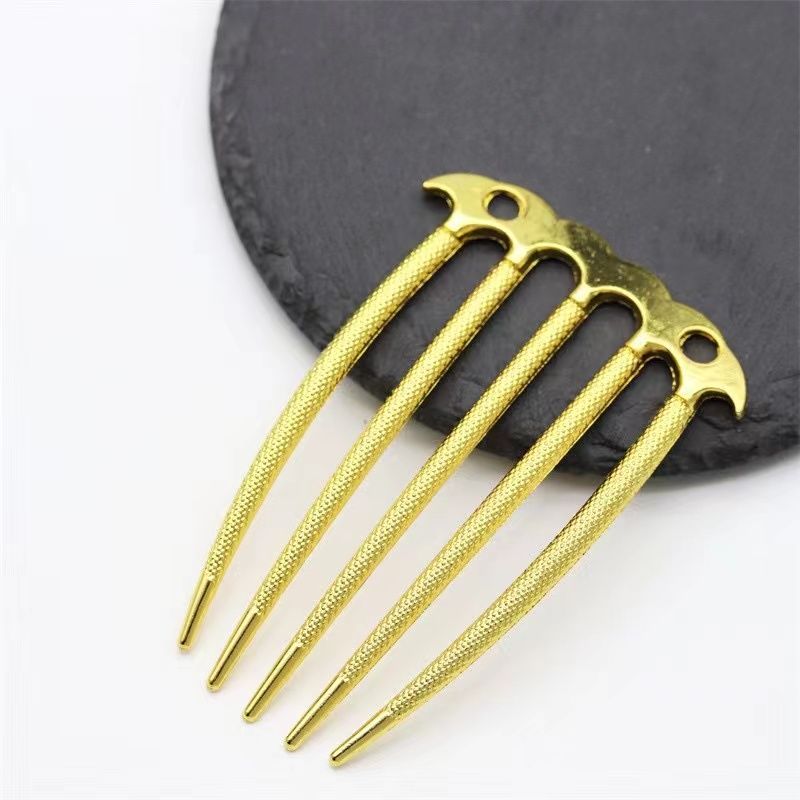 A gold textured five-prong metal hair comb showing the knurled detail on the tines and pierced top.