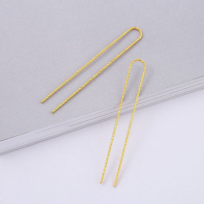 A pair of 75mm gold-tone U-shaped hair forks with a textured finish, shown on a light grey background.