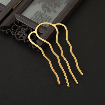 Close-up of a gold four-prong alloy hair pin with wavy design, placed on a dark surface with a decorative frame, ideal for DIY crafts.