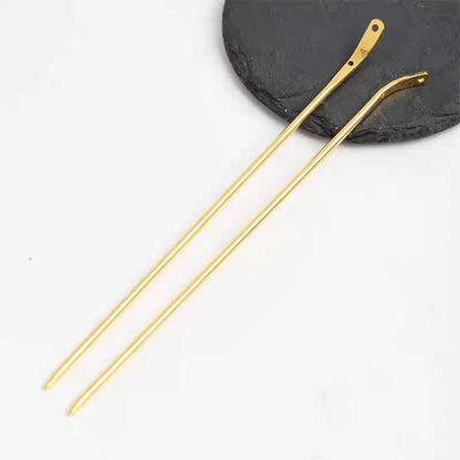 A pair of gold curved metal hair sticks for DIY crafts, displayed on a dark slate coaster.