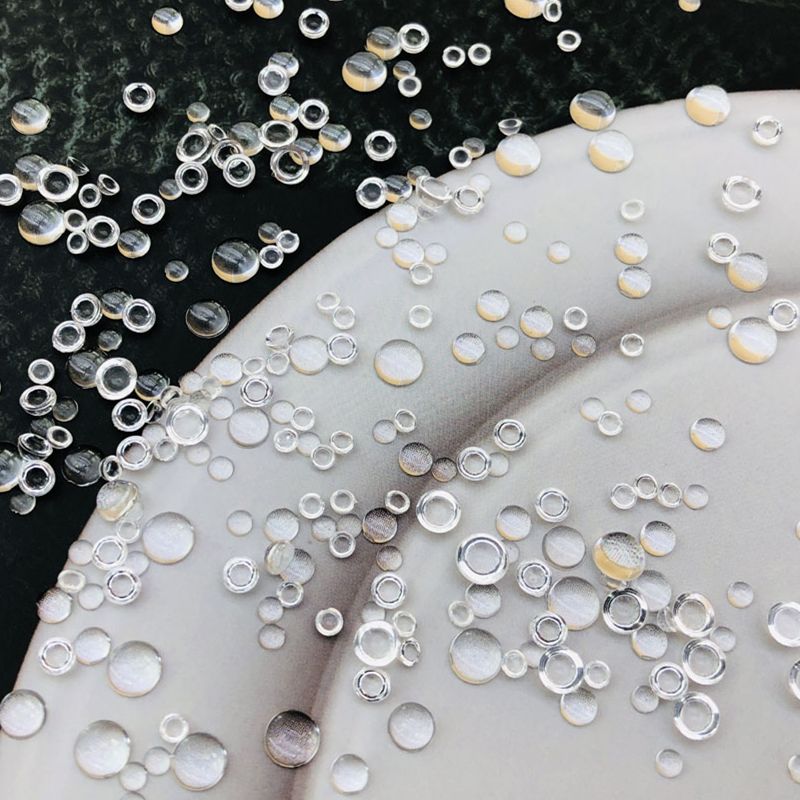 Mixed size clear acrylic dew drop cabochons scattered on white plate showing realistic water droplet effect