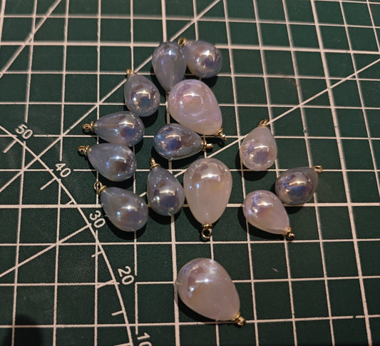 Collection of various sized blue and white mermaid tear drop jewelry making charms on a craft mat with ruler markings.