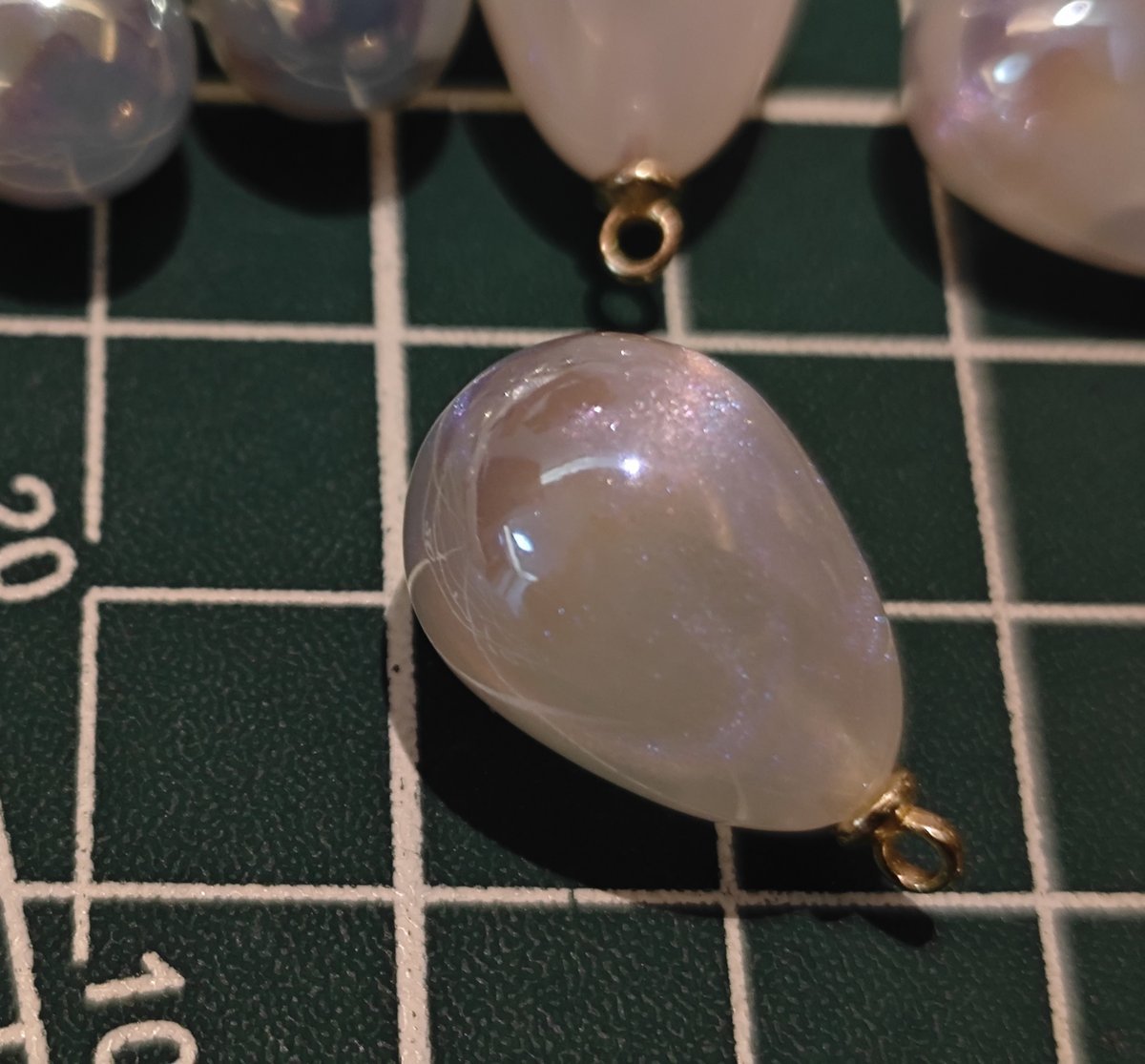Macro shot of a single white pearlescent charm showing fine internal glitter and teardrop shape for DIY supplies.