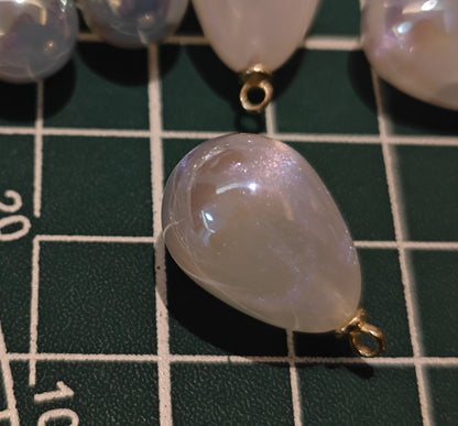 Macro shot of a single white pearlescent charm showing fine internal glitter and teardrop shape for DIY supplies.