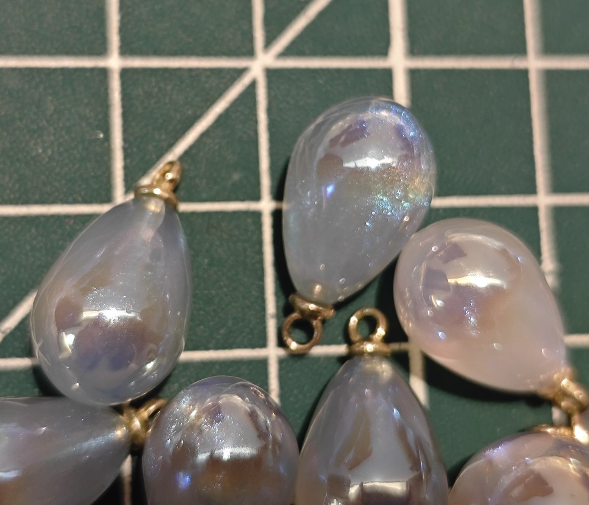 Assortment of blue and white pearlescent teardrop charms with gold findings, showing fine shimmer detail.