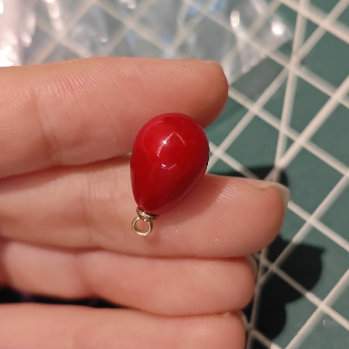 Close-up of a single Angola Red plastic tear drop charm held between fingers, showing glossy finish for handmade jewelry.