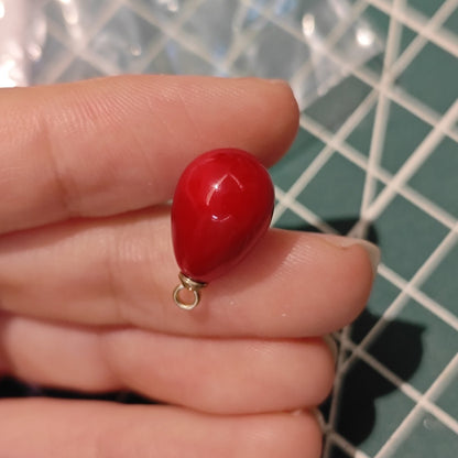 Close-up of a single Angola Red plastic tear drop charm held between fingers, showing glossy finish for handmade jewelry.