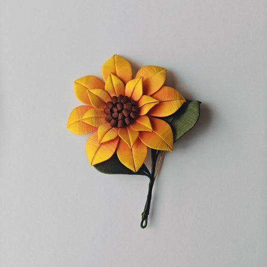 Luxury 3D embroidery floral pin depicting a bright sunflower with a green leaf made through artisanal thread-wrapping techniques.