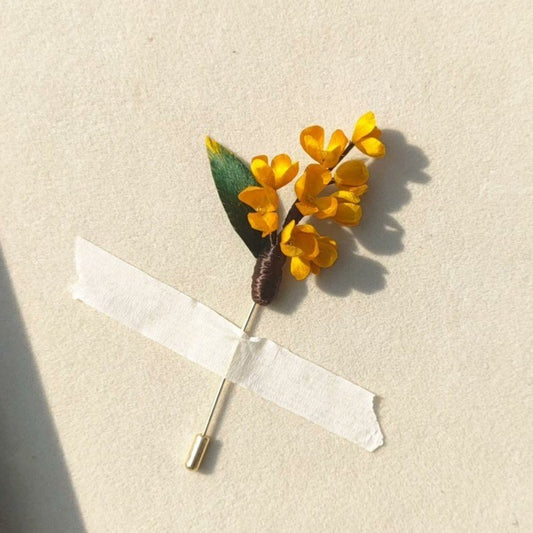 3D silk velvet floral lapel pin depicting a branch of yellow osmanthus flowers made with traditional artisanal Ronghua techniques.