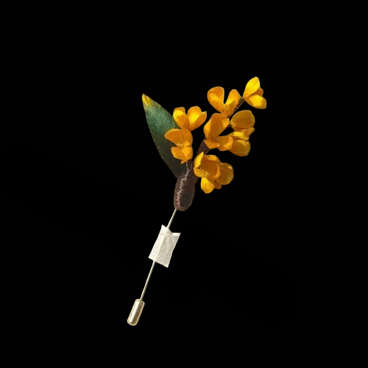 Handcrafted golden Osmanthus Ronghua brooch featuring tiny velvet-textured silk blossoms and a green leaf on a long gold-tone pin.