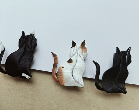 Three handcrafted Chanhua cat brooches in black, calico, and tuxedo patterns, made with artisanal thread-wrapping.