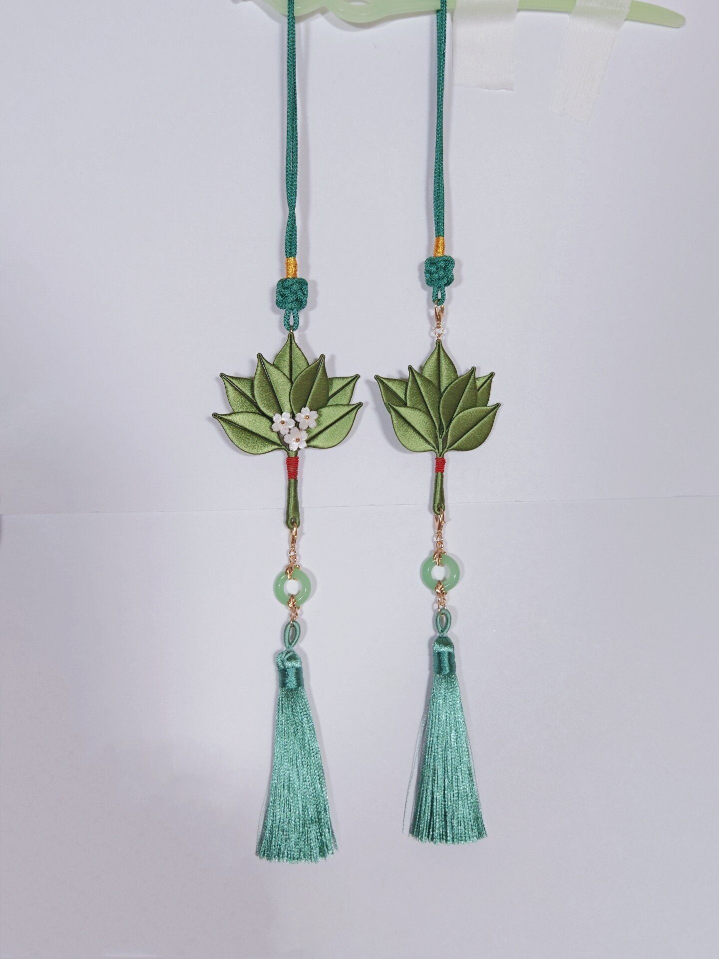 Chanhua handmade pomelo leaf pendants in two styles — with and without white flower accents — each with a jade ring and green silk tassel, hanging against a white background