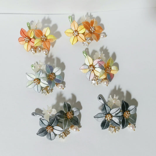 Chanhua Shijing handmade flower brooches in six color combinations including orange, yellow, blue-grey, pastel multicolor, dark grey, and charcoal, displayed on a white background