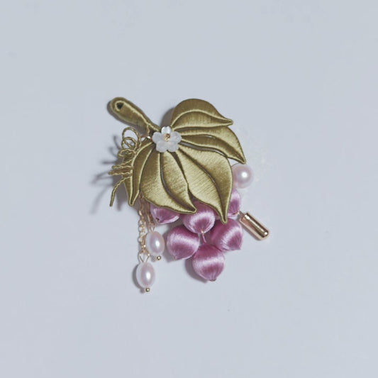 
Chanhua handmade grape brooch with purple-pink grape cluster, gold-green leaf, small white flower accent, and pearl drop on a gold chain, displayed on a light gray background