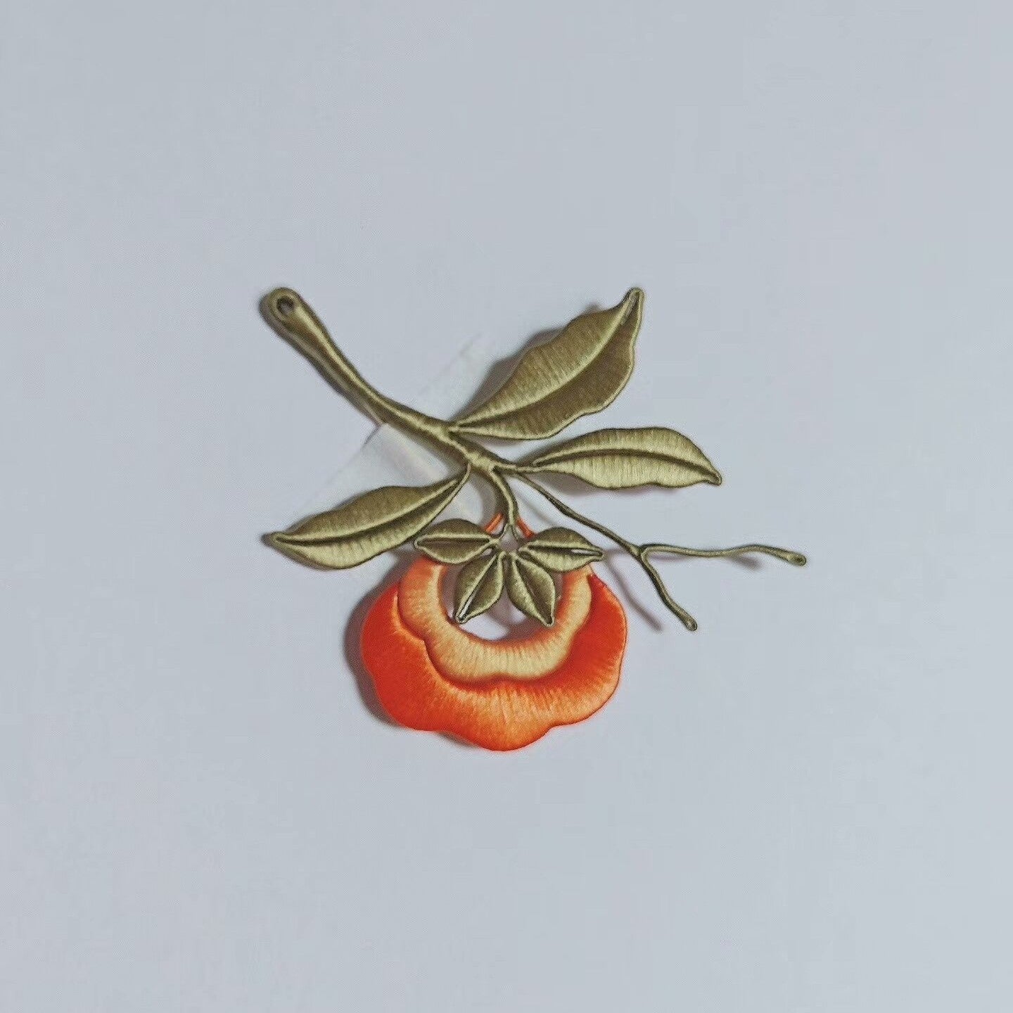 Chanhua handmade persimmon brooch with orange fruit, olive-green branch, multiple leaves, and bare twig tips, displayed on a light gray background